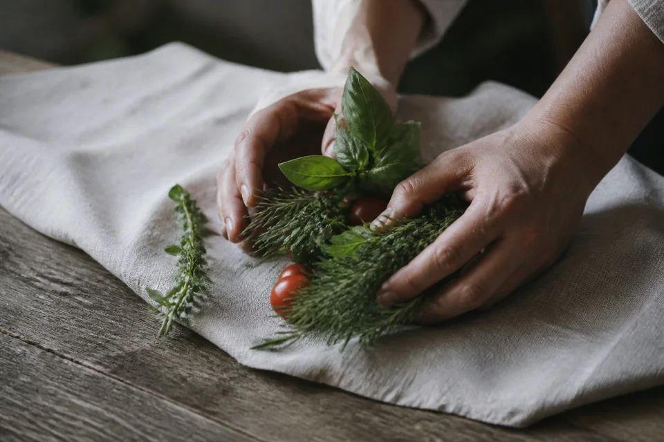 Hands gathering fresh herbs and tomatoes on a linen cloth.