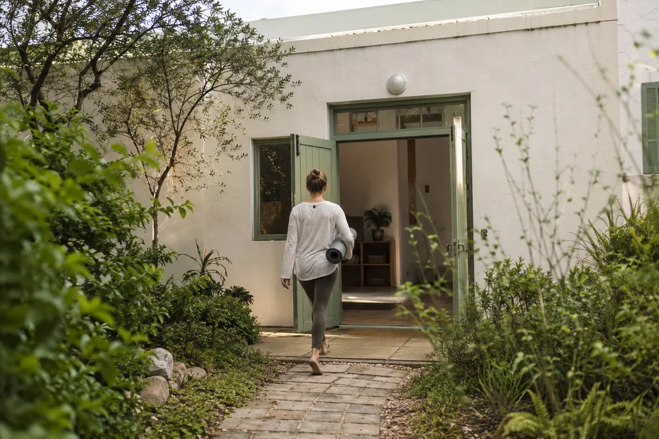 A person carrying a yoga mat towards an open studio doorway.